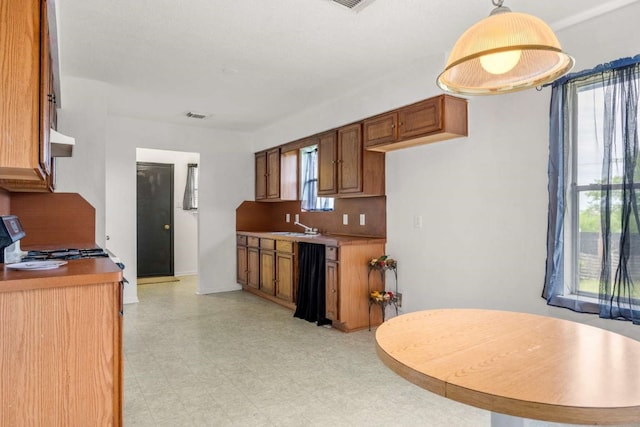 kitchen featuring stove, decorative light fixtures, light tile flooring, backsplash, and sink