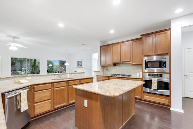 kitchen with brown cabinetry, decorative backsplash, appliances with stainless steel finishes, pendant lighting, and a sink