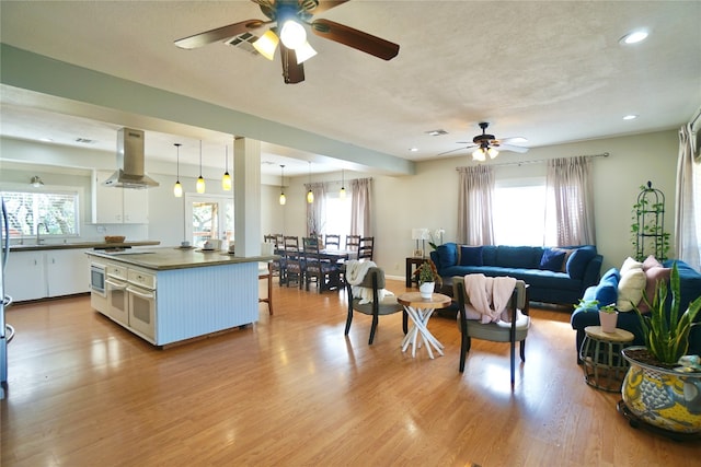 kitchen featuring ceiling fan, white cabinetry, light hardwood / wood-style flooring, and wall chimney range hood