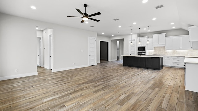 kitchen with light hardwood / wood-style floors, a center island, stainless steel microwave, hanging light fixtures, and white cabinetry