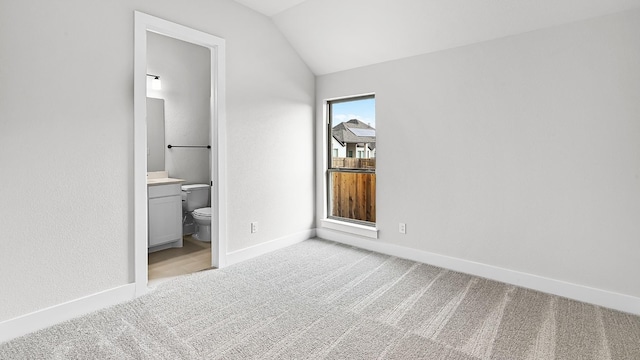 unfurnished bedroom featuring ensuite bath, light carpet, and vaulted ceiling