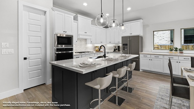 kitchen featuring a kitchen island with sink, stainless steel appliances, sink, and white cabinets