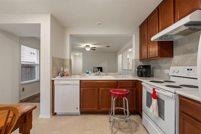 kitchen featuring backsplash, under cabinet range hood, light countertops, white appliances, and a sink