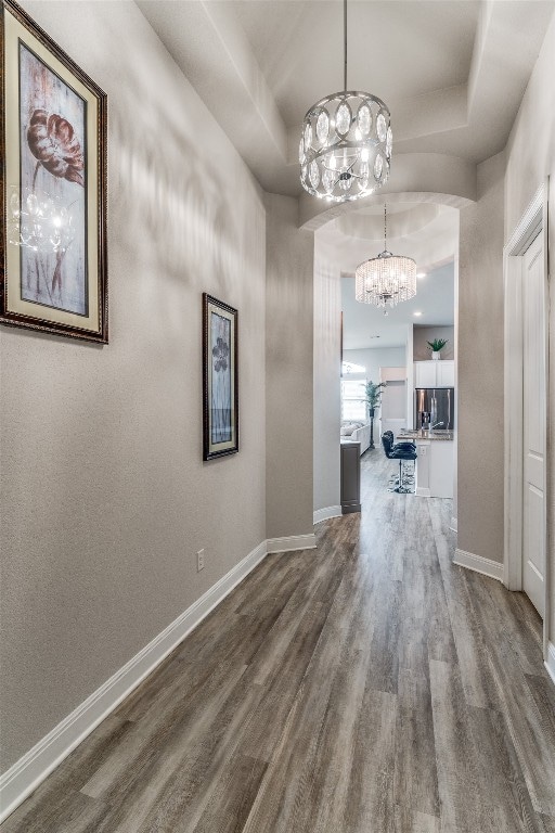 corridor with hardwood / wood-style floors, a notable chandelier, and a tray ceiling