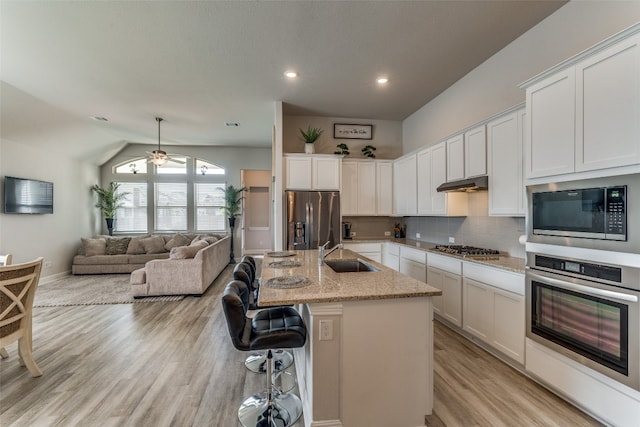 kitchen with appliances with stainless steel finishes, lofted ceiling, an island with sink, white cabinets, and light wood-type flooring