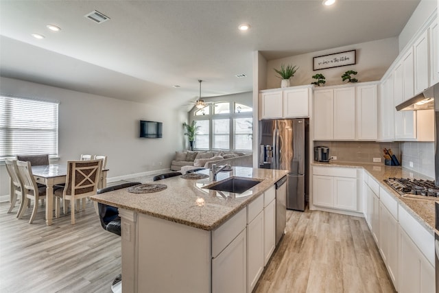 kitchen with light stone countertops, backsplash, a center island with sink, white cabinetry, and light wood-type flooring