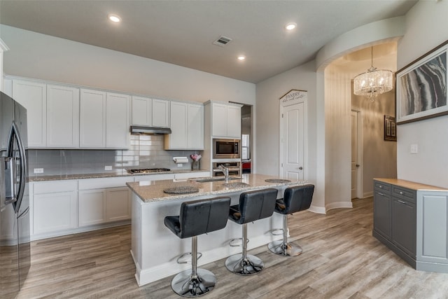 kitchen featuring appliances with stainless steel finishes, light hardwood / wood-style flooring, tasteful backsplash, an island with sink, and white cabinetry