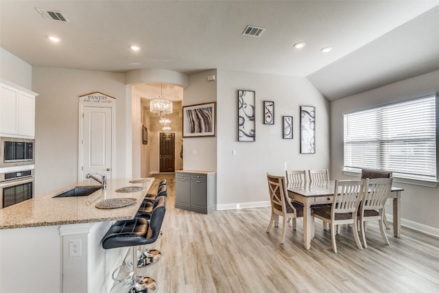 dining area with an inviting chandelier, light hardwood / wood-style flooring, vaulted ceiling, and sink