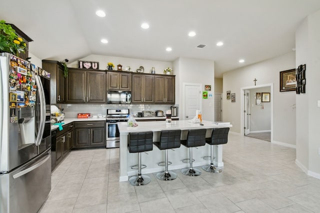 kitchen featuring a breakfast bar, tasteful backsplash, stainless steel appliances, vaulted ceiling, and an island with sink