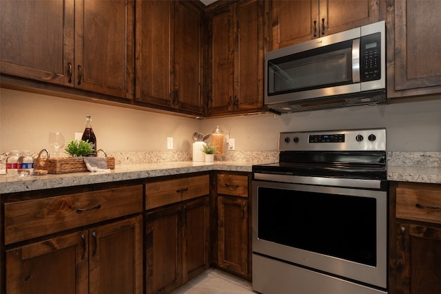 kitchen with appliances with stainless steel finishes, dark brown cabinetry, and light stone counters