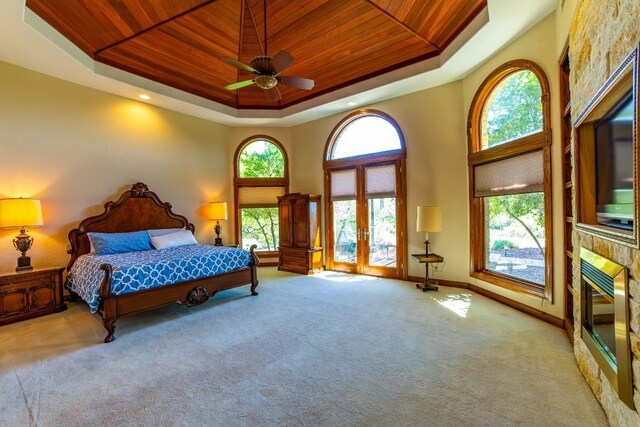 carpeted bedroom with a raised ceiling, wooden ceiling, a high ceiling, french doors, and ceiling fan