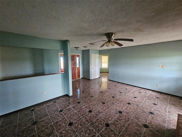 empty room featuring a textured ceiling, dark tile flooring, and ceiling fan