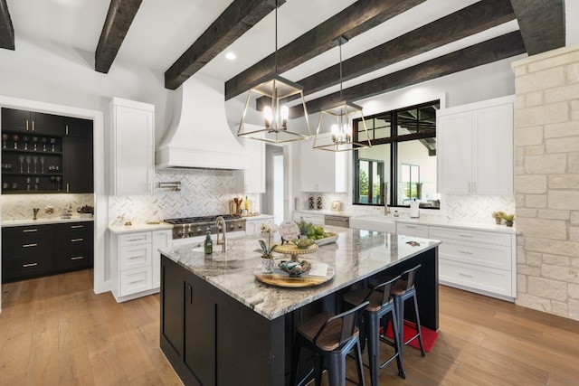 kitchen featuring custom exhaust hood, white cabinetry, hanging light fixtures, a kitchen breakfast bar, and a kitchen island with sink