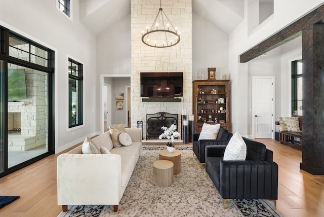 living room with a stone fireplace, a towering ceiling, a notable chandelier, and light hardwood / wood-style flooring