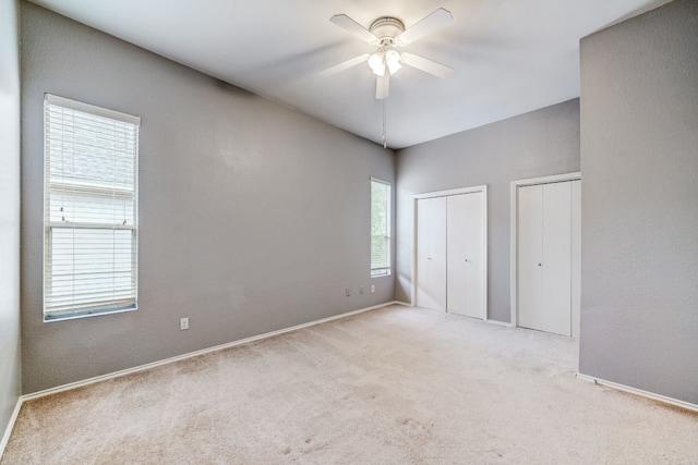 unfurnished bedroom featuring light colored carpet, ceiling fan, two closets, and multiple windows