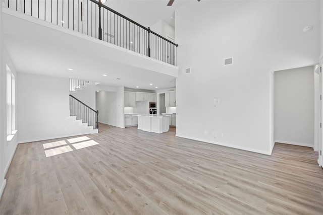 unfurnished living room featuring a towering ceiling, light hardwood / wood-style floors, and ceiling fan