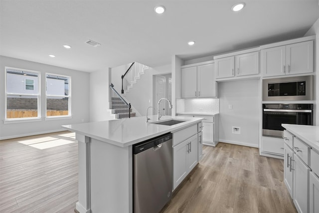 kitchen featuring stainless steel appliances, an island with sink, white cabinets, decorative backsplash, and light wood-type flooring