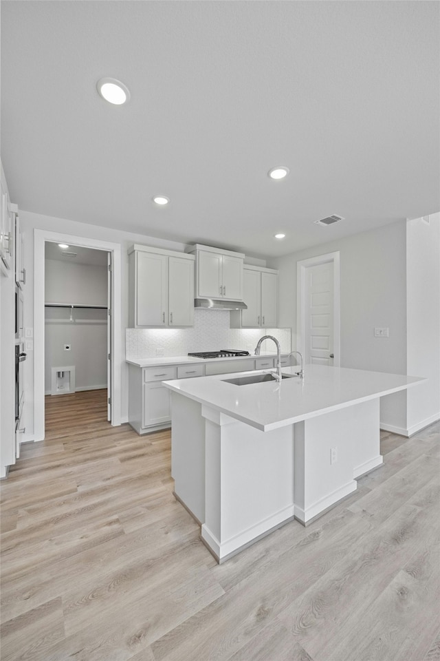 kitchen featuring sink, tasteful backsplash, light wood-type flooring, a kitchen island with sink, and white cabinets