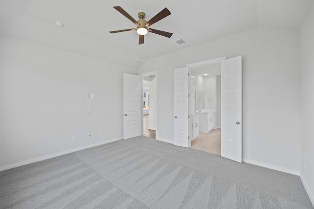 unfurnished bedroom featuring ceiling fan, ensuite bathroom, vaulted ceiling, and light carpet