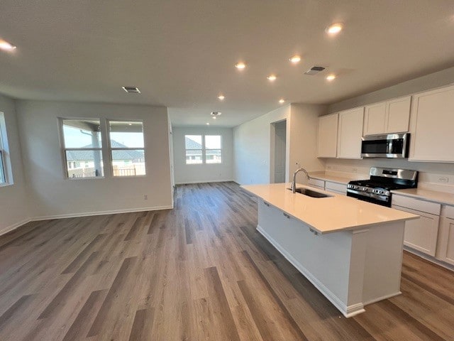 kitchen with sink, hardwood / wood-style flooring, stainless steel appliances, a center island with sink, and white cabinets