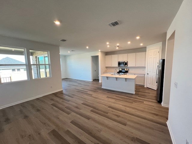 kitchen with appliances with stainless steel finishes, sink, a kitchen island with sink, white cabinets, and dark wood-type flooring