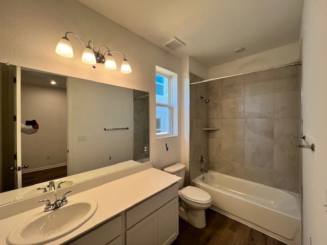 full bathroom with wood-type flooring, toilet, tiled shower / bath, and vanity