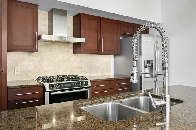 kitchen with dark stone counters, appliances with stainless steel finishes, and wall chimney range hood