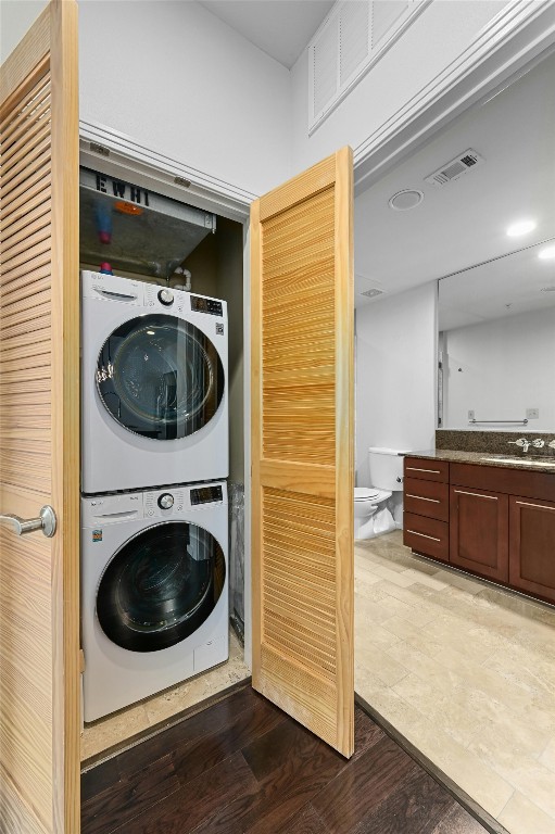 clothes washing area featuring sink, dark wood-type flooring, and stacked washing maching and dryer