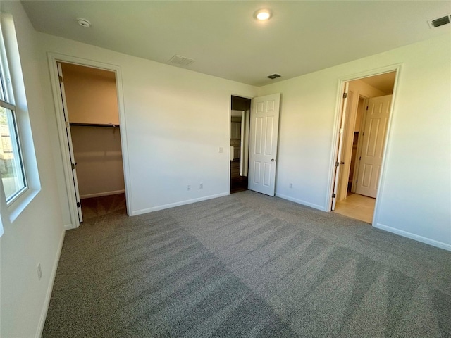 unfurnished bedroom featuring light carpet, a walk in closet, and a closet