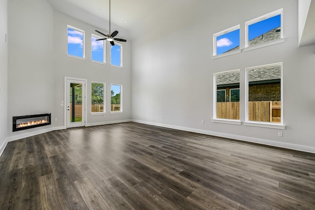 unfurnished living room with a towering ceiling, ceiling fan, and dark hardwood / wood-style floors