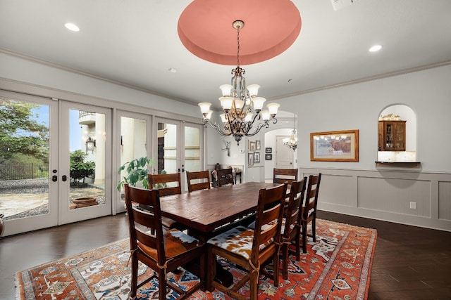 dining area featuring a wainscoted wall, ornamental molding, dark wood-style flooring, an inviting chandelier, and french doors