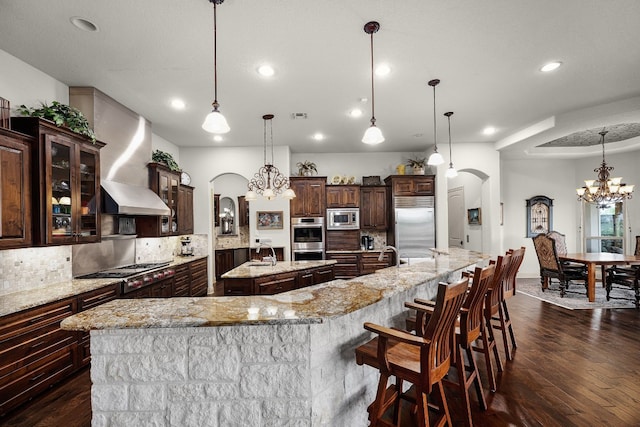 kitchen with glass insert cabinets, arched walkways, a large island, and built in appliances