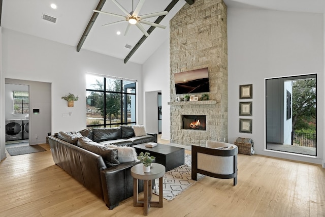 living room with a stone fireplace, high vaulted ceiling, plenty of natural light, and washing machine and dryer