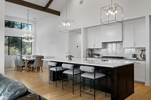 kitchen featuring white cabinetry, a healthy amount of sunlight, an inviting chandelier, and a center island with sink