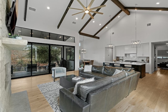 living room with a fireplace, high vaulted ceiling, ceiling fan with notable chandelier, beam ceiling, and light hardwood / wood-style floors