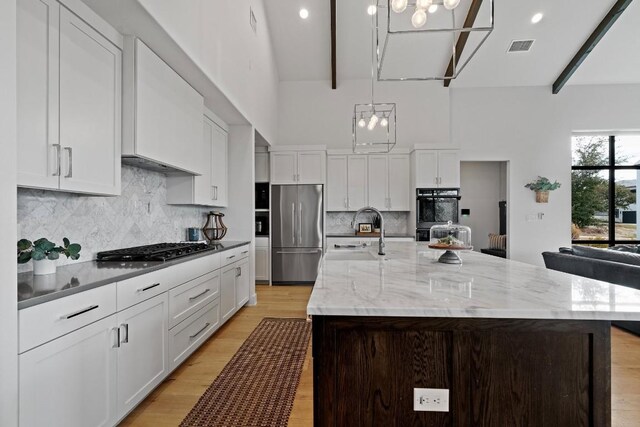 kitchen featuring a large island with sink, sink, stainless steel appliances, and a notable chandelier