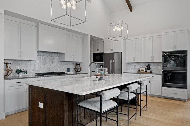 kitchen with black appliances, sink, a chandelier, a large island, and light wood-type flooring