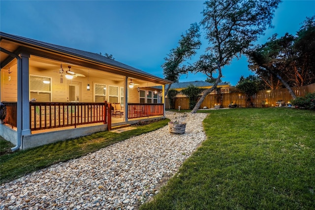 yard at dusk with ceiling fan and covered porch