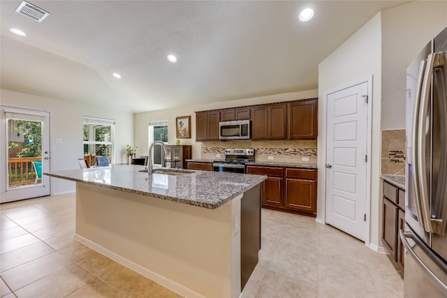 kitchen featuring appliances with stainless steel finishes, light stone counters, vaulted ceiling, sink, and a center island with sink