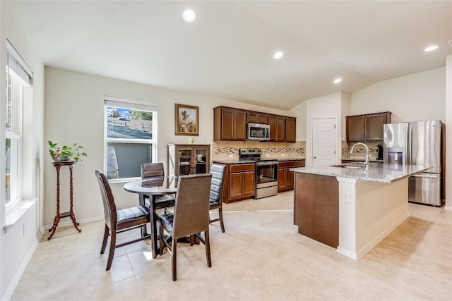 kitchen featuring decorative backsplash, stainless steel appliances, sink, lofted ceiling, and an island with sink