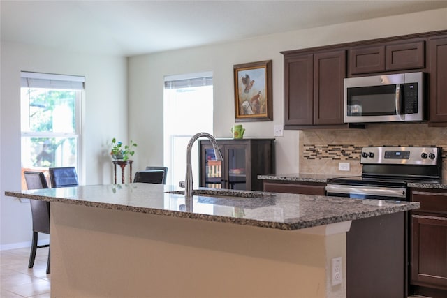 kitchen with appliances with stainless steel finishes, stone countertops, a kitchen island with sink, and sink