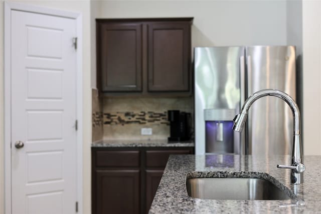 kitchen with sink, backsplash, stainless steel fridge, stone countertops, and dark brown cabinets