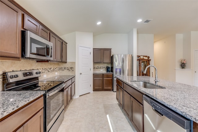 kitchen with sink, light stone counters, decorative backsplash, light tile patterned floors, and appliances with stainless steel finishes