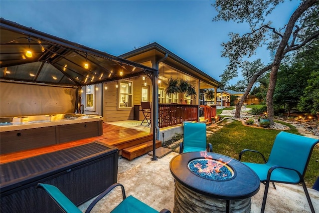 patio terrace at dusk with a fire pit, a yard, a wooden deck, and a hot tub