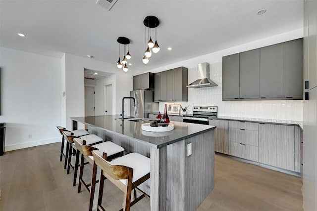 kitchen with gray cabinets, pendant lighting, light hardwood / wood-style floors, stainless steel appliances, and wall chimney exhaust hood