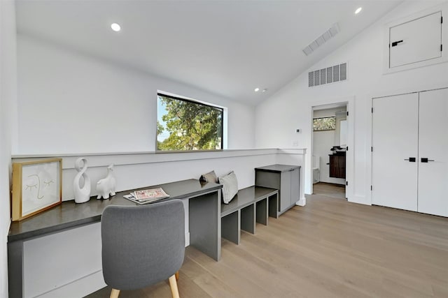 office featuring lofted ceiling, built in desk, and light hardwood / wood-style flooring