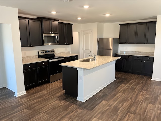 kitchen featuring light stone counters, a center island with sink, stainless steel appliances, and dark hardwood / wood-style floors