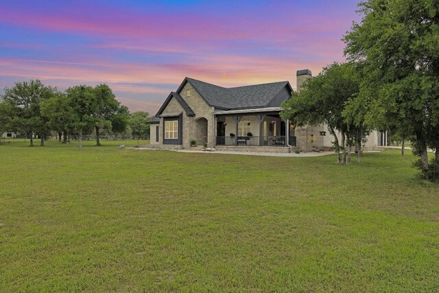 back house at dusk featuring a lawn and a porch