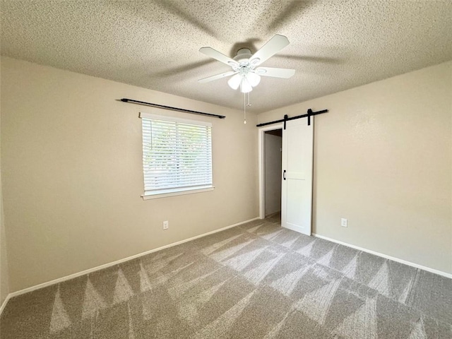 unfurnished bedroom featuring a barn door, ceiling fan, carpet, and a textured ceiling