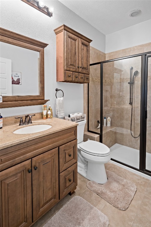 bathroom featuring a shower with door, tile floors, vanity, and toilet